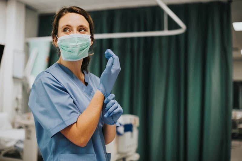 Female Nurse With Mask Putting Gloves