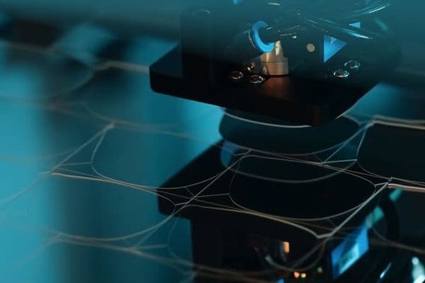 Close-up of a machine with a blue light, creating a delicate, web-like structure on a dark surface.