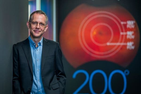 Alexandre Montague, a man in a suit and blue shirt, smiles in front of a red graphic of an eye and "200°