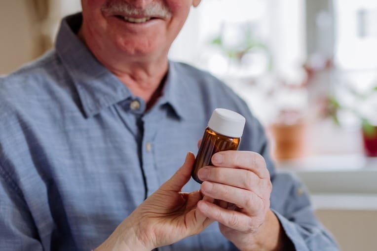 a senior man holding a bottle containing medication