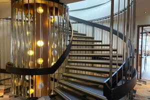 A modern spiral staircase with dark treads and metal railings next to a cylindrical light feature.